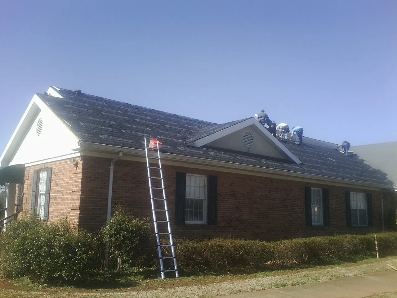 Crew tearing shingles off a brick ranch roof with a ladder set — Emergency Roof Repair work by our crew in La Crescenta