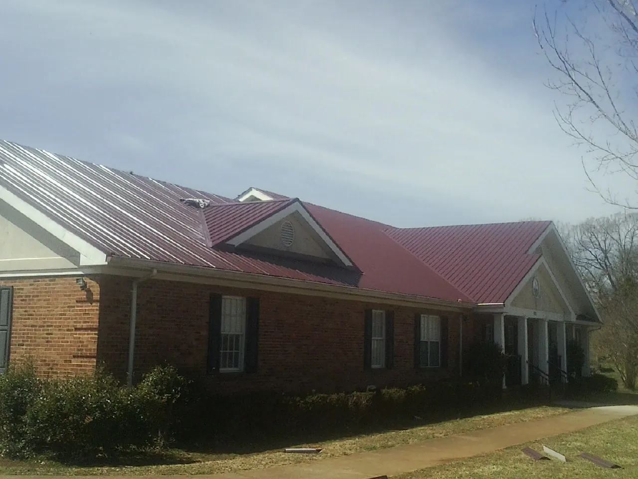 Red metal roof with gabled entries on a long brick building, from a Hail Damage Roof Repair job in La Crescenta