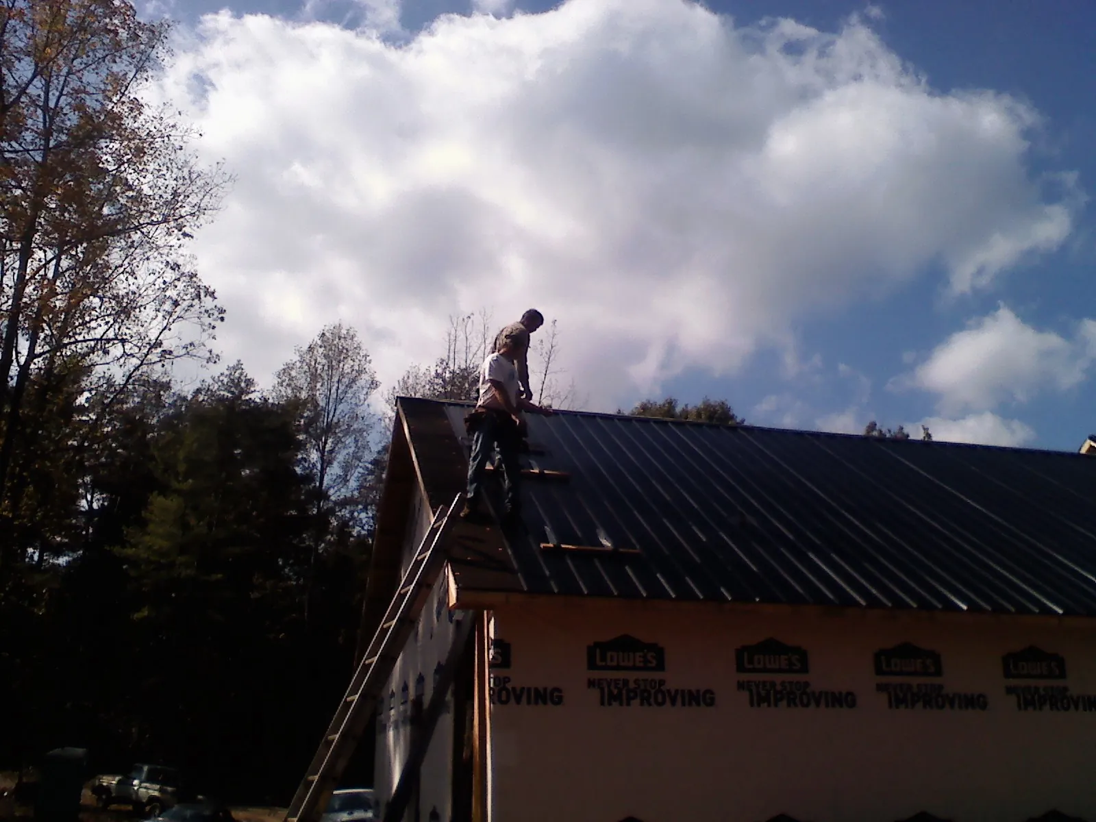 Roofer fastening dark metal panels high against a cloudy sky, from a Roof Inspection job in La Crescenta