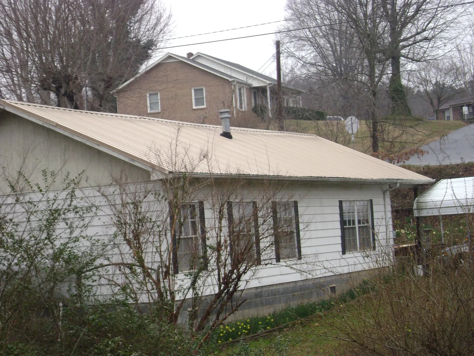 Tan metal roof on a white sided house set into a hillside — Commercial Roofing by Roofing Brothers in La Crescenta